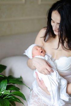 Young black haired mother wearing white clothes holding newborn baby. Concept of motherhood and happiness.