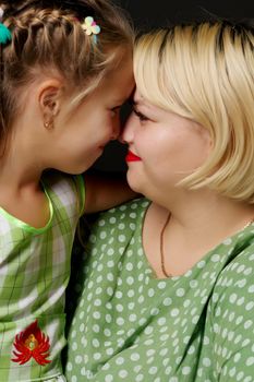 Happy family mom and daughter are hugging on a black background in the studio.