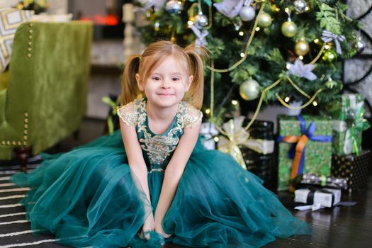 Little beautiful girl wearing blue dress standing near Christmas tree. Concept of celebrating New Year, fashion and childhood.