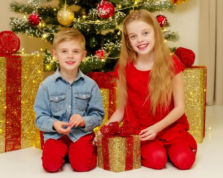 Boy and girl near the Christmas tree decorated with toys and gifts on Christmas Eve. Holiday concept.