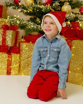 A cute little boy near a Christmas tree with a gift. Concept of family holidays, Happy childhood.