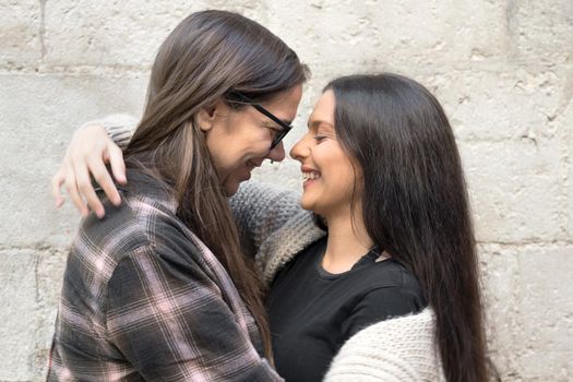 Portrait of an affectionate young lesbian couple hugging each other while standing together in front of a stone wall outside. High quality photo.