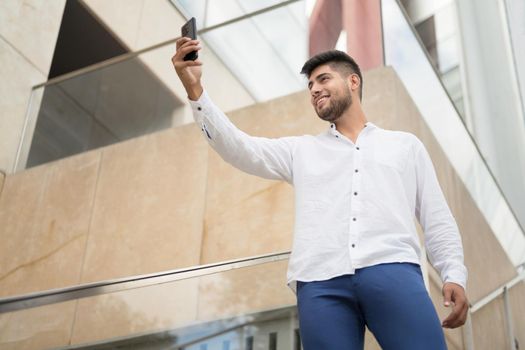 Young handsome hispanic man taking selfie with smartphone outdoors. High quality photo