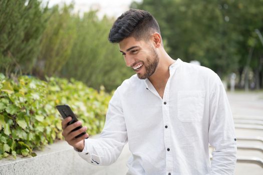 Handsome young man, smiling, using a mobile phone outdoors. High quality photo