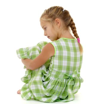 Beautiful little girl is sitting on the floor in the studio. The concept of a happy childhood, beauty and fashion. Isolated on white background.