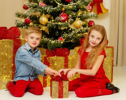 Boy and girl near the Christmas tree decorated with toys and gifts on Christmas Eve. Holiday concept.