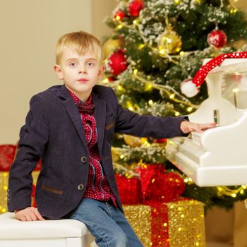 A cute little boy is playing on a white piano in a dark room by candlelight. Concept Christmas and New Year, holidays.