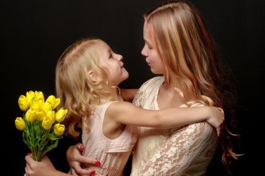 Two beautiful little girls with flowers in the studio. The concept of happy people, children.