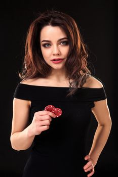 Smiling girl holding a gambling chips in her hands on black background. Sexy brunette in a dress. Poker.