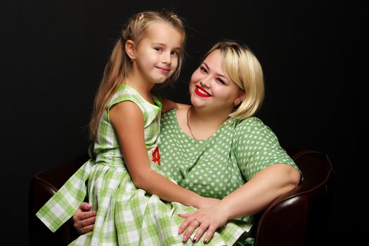 Happy family mom and daughter are hugging on a black background in the studio.