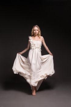 Photo of a dancing beautiful young girl in white wedding dress over dark background