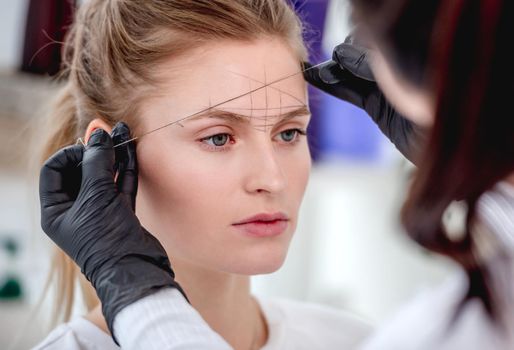 Permanent tattoo makeup master defines the ideal eyebrow shape with professional tools. Closeup view of microblading work process