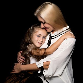 Beautiful young mother with a little daughter in her arms, studio on a black background. The concept of a happy childhood, advertising.