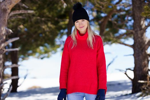 Young blonde woman in a snowy forest in the mountains, in Sierra Nevada, Granada, Spain. Female wearing winter clothes.