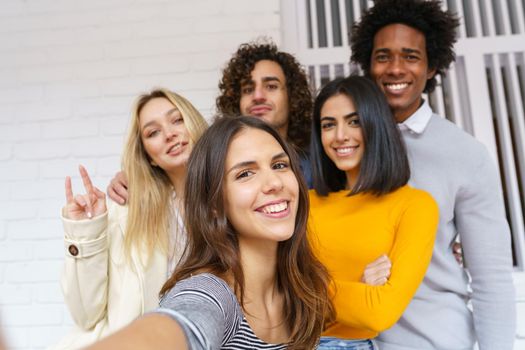 Multi-ethnic group of friends taking a selfie together while having fun in the street. Caucasian girl in the foreground.