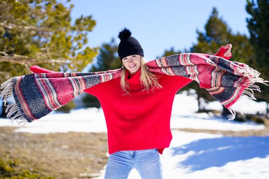 Young happy young blonde woman waving her scarf in the wind in a forest in the snowy mountains in Sierra Nevada, Granada, Andalusia, Spain