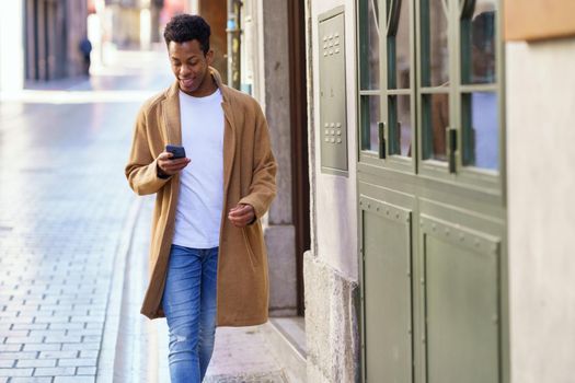 Young black man using his smartphone outdoors. Cuban guy smiling in urban background.