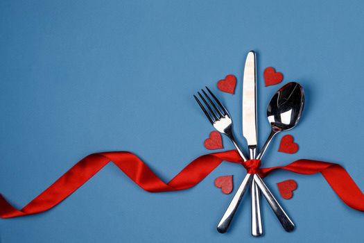 Cutlery set tied with red silk ribbon and hearts on blue background Valentine day dinner concept