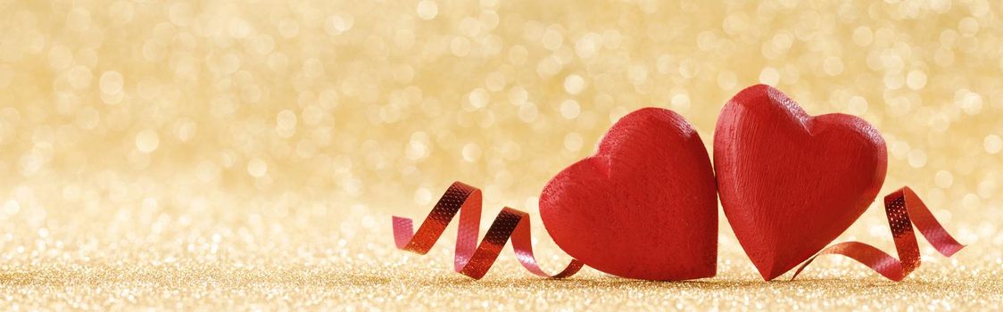 Two red handmade wooden hearts and ribbons on golden bright glitter lights bokeh background Valentines day