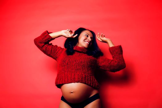 close up portrait of pregnant woman with big belly, hands hold, red sweater on background, choise of gender, lifestyle people concept