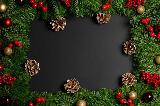 Christmas Border frame of tree branches on black background with copy space , baubles, holly berries, pine cones