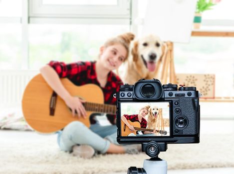 Smiling teenage girl playing guitar in bright room. Blogger profession. Shooting with a camera for a blog