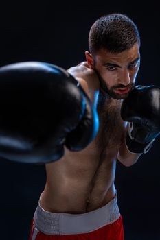 Portrait of tough male boxer posing in boxing stance against black background. Professional fighter ready for boxing match.