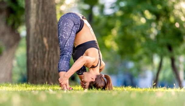 Beautiful girl doing yoga workout at nature and keeping her body down . Young woman exercising and stretching outdoors in the morning