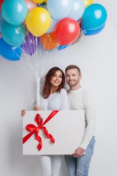 Young smiling couple with balloons and big gift box, Valentine day birthday surprise concept