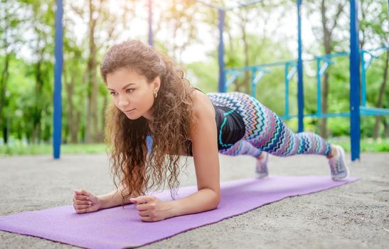 Sport girl doing plank exercise on yoga mat outdoors at summer. Young woman during workout at stadium