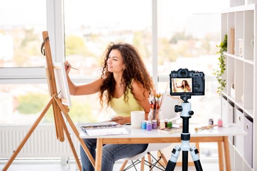 Cute girl painter making new picture sitting in workshop. Blogger profession. Shooting with a camera for a blog