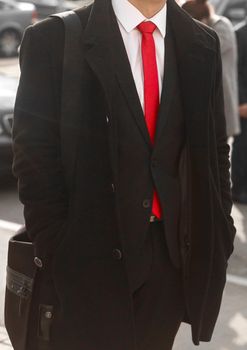 Black men's coat and suit with white shirt and red tie close-up.
