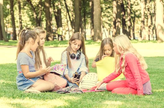 Friendly teens sitting with notebooks on the grass in the park