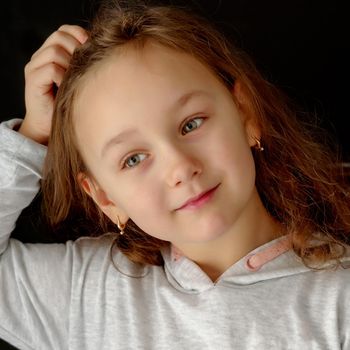 A beautiful little girl straightens her hair on her head. The concept of beauty and fashion, photo on the cover of the magazine.Studio portrait on black background.