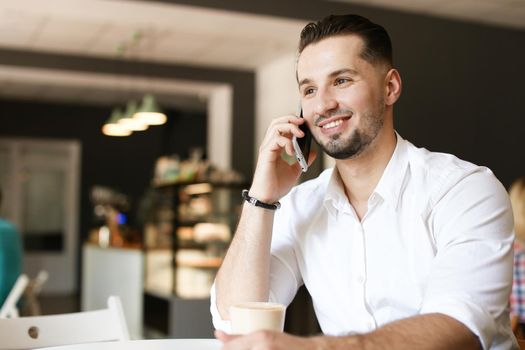 Young businessman talking by smartphone at cafe. Concept of modern technology and businessperson.