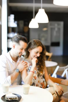 Young caucasian man hugging woman at cafe, ,sitting near cups of coffee. Concept of positive emotions, feelings and resting on lunch.