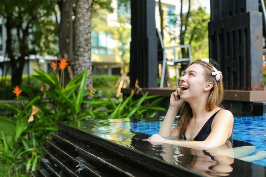 sunshine portrait of happy beautiful woman talking on smart phone swimming at pool. concept of international calls, travel and resting time