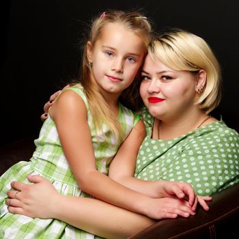 Happy family mom and daughter are hugging on a black background in the studio.