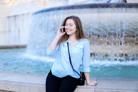 Young businesswoman speaking by smartphone in Trevi fountain background. Concept of modern technology, advantageous tariff plan and summer vacations in Europe.