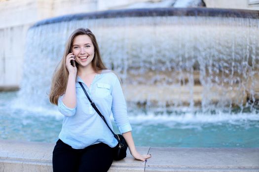 Young woman talking by smartphone in Trevi fountain background. Concept of modern technology, advantageous tariff plan and summer vacations in Europe.