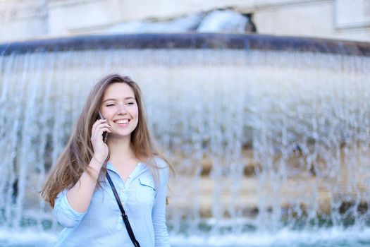 Young caucasian student speaking by smartphone in Trevi fountain background. Concept of modern technology, advantageous tariff plan and summer vacations in Europe.