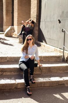 Young female tourist sitting on stairs inside Colosseum, Italy. Concept of visiting famous italian landmarks and exursions.