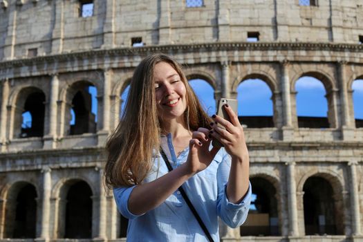 Young woman browsing by smartphone in Colosseum background in Rome, Italy. Concept of last minute tours to Italy and using Internet by modern gadget for social networks.