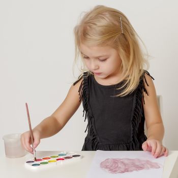 Little girl draws paints on a sheet of paper. Concept kindergarten, montessori education.