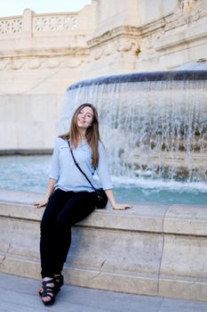 Young businesswoman sitting near Trevi fountain, wearing blue shirt. Concept of traveling to Italy, Rome and youth.