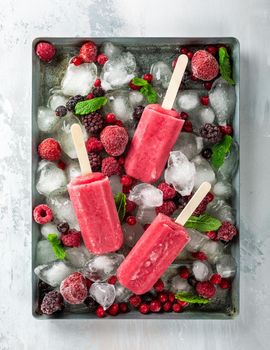 Homemade strawberry popsicles on metal plate with ice, assorted berries and mint. Healthy summer food concept. Top view