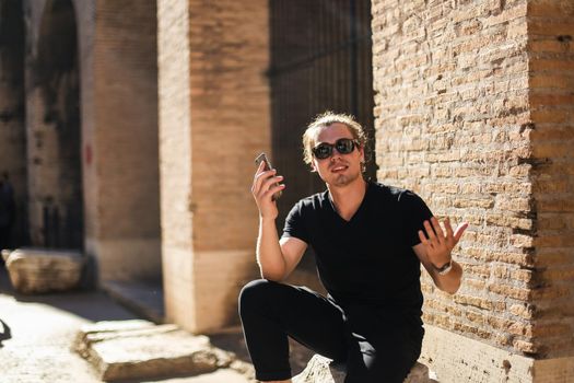 Young male tourist using smartphone inside Colosseum in Rome, Italy. Concept of modern technology, tourism and last minute tours to Europe.