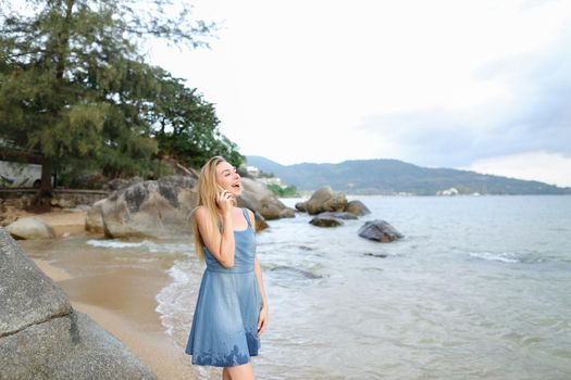 Young girl speaking by smartphone on morning sea shore. Concept of modern technology and exotic summer vacations.