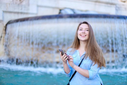 Young caucasian student chatting by smartphone in Trevi fountain background. Concept of modern technology, advantageous tariff plan and summer vacations in Europe.