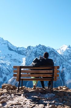 High quality photo about a couple of lovers are sitting on a bench in the mountains, a view from the back, rocks in the snow, a man and a woman